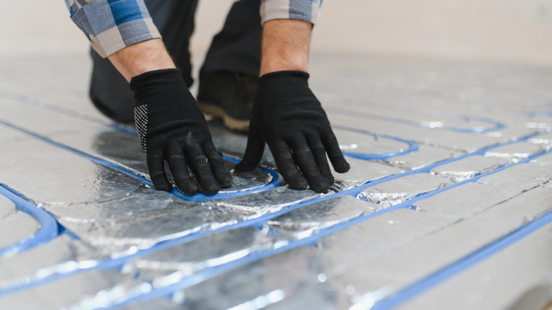Person wearing black protective gloves installing underfloor heating