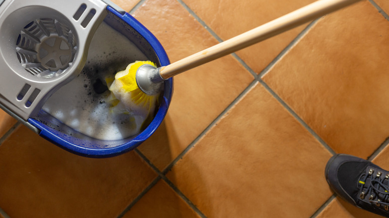 A person cleaning a tiled floor with a mop and a bucket of soapy water