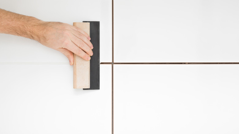 Person grouting white tiles with dark grout