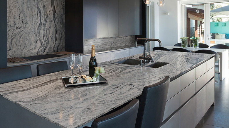 A kitchen island covered in a granite with two sinks and a champagne offering on top