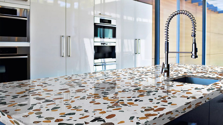A kitchen island made out of chunky terrazzo with four ovens in the bacjground
