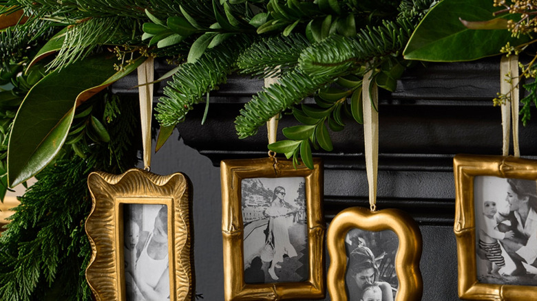 Four gold ornament frames hang from a greenery-covered mantle