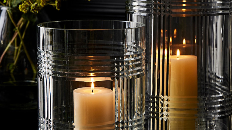 Two cream candles are held in cut glass hurricane holders situated on a black table