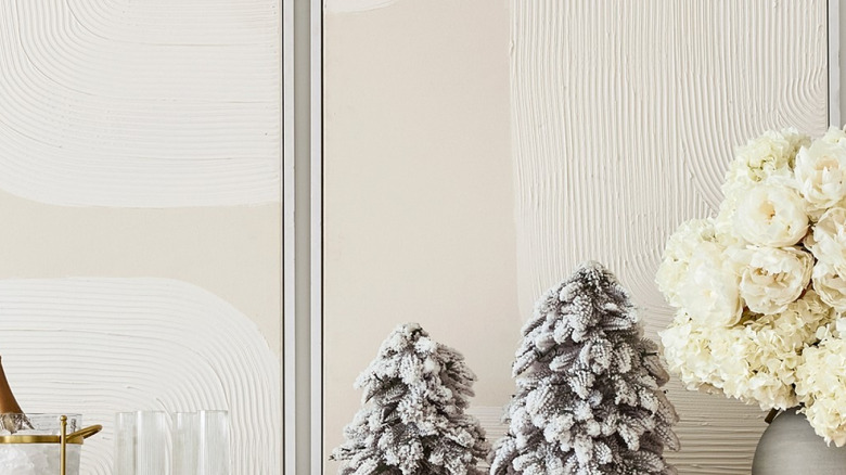A cream sideboard is decorated with white flocked tabletop trees, florals, and a garland