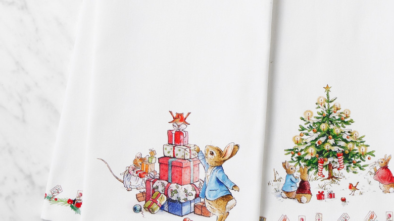 Two tea towels with images from Beatrix Potter's Peter Rabbit tales are shown on a white marble countertop