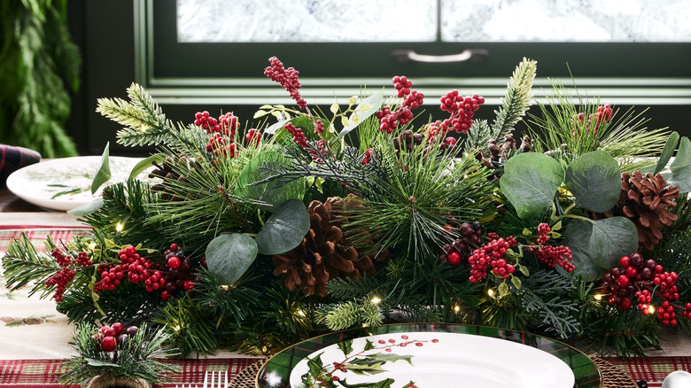 A Williams Sonoma Faux Noel Centerpiece sits on an elegant table next to a place-setting and red glassware