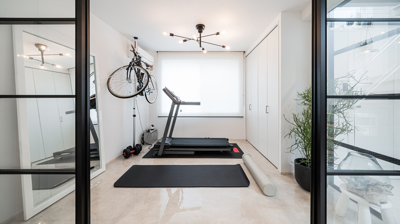 A home gym with yoga mat, treadmill, weights, and a bike hanging from the ceiling with a large mirror on one side.