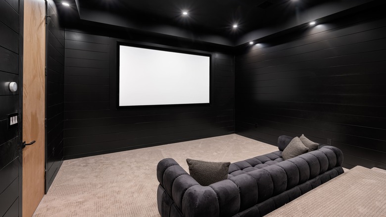 A home theater room with large wall-mounted screen and plush sofa seating.