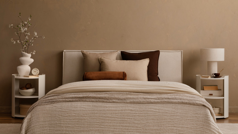 A smart bedroom with taupe walls, bed with brown bedding and multiple cushions in different shades of brown.