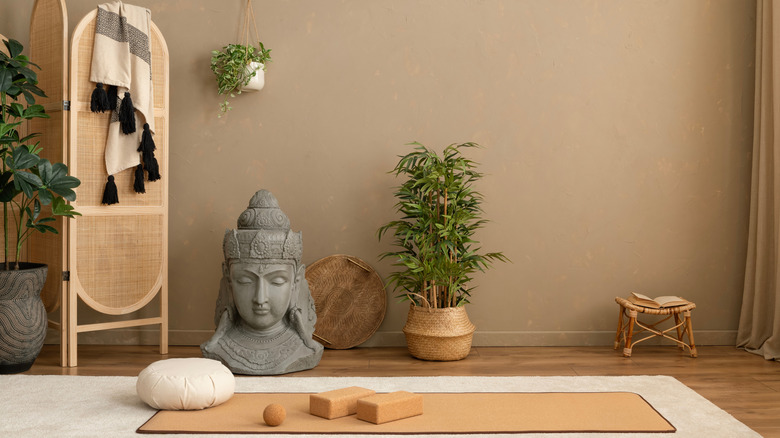 A room with yoga mat, potted plants, and a large Buddha statue on the floor.