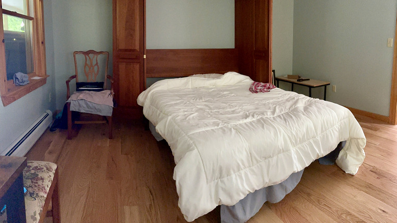 A room with a murphy bed, bedside chair, and small table