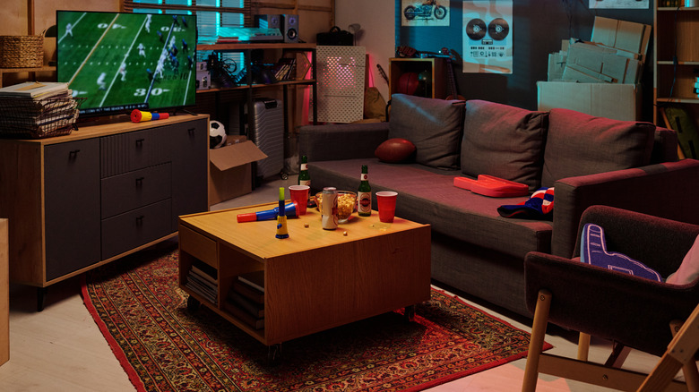 A people place with TV showing American football, a big sofa, and a coffee table with beer and snacks on it.