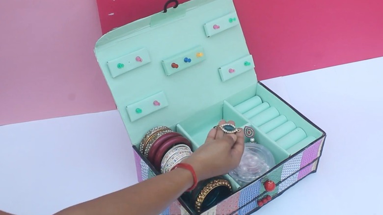 Woman holding earring over a jewelry box made from a shoe box