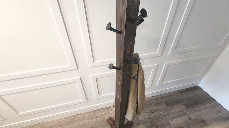 Simple freestanding wood coat rack with railroad spikes as the hooks next to a white wall