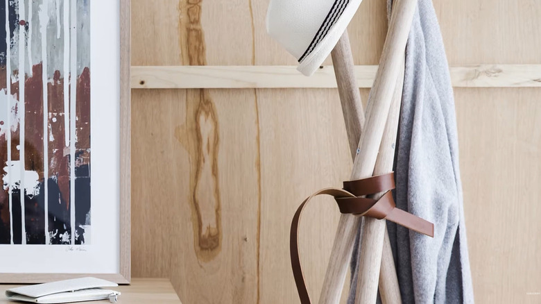 Tripod-style coat rack made with three poles and a leather strap wrapped around it
