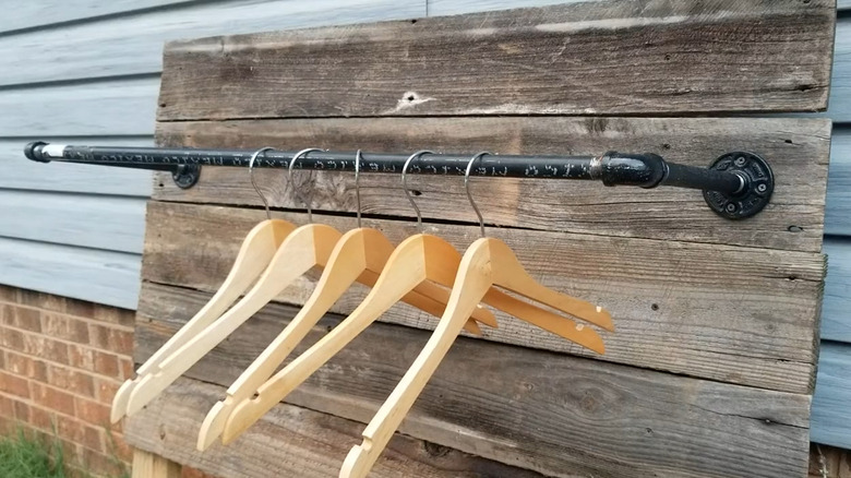 Black pipe attached to a wooden background to create a coat rack with hangers on it
