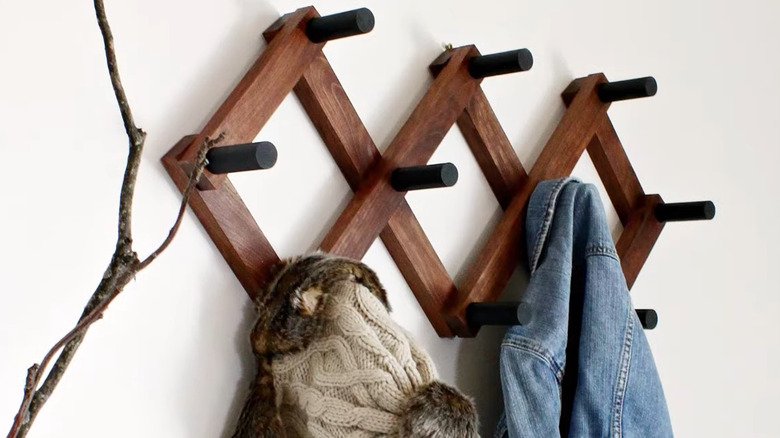 DIY accordion-style coat rack with thick pegs hanging on a white wall with a coat and hat on it