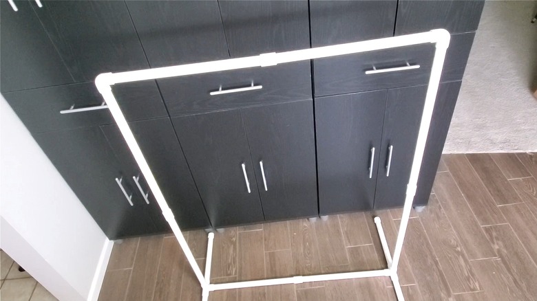 DIY garment rack made with white PVC pipe sitting next to a black cabinet