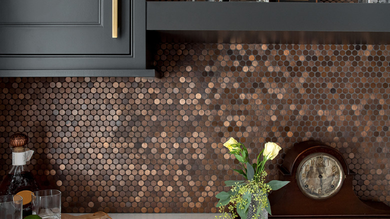 Kitchen backsplash made of pennies with black cabinets, clock, and flowers