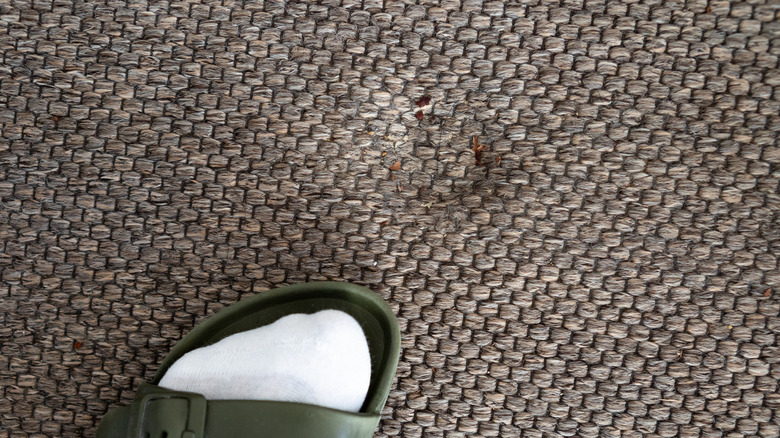 A person's foot near a deep furniture indentation in carpet