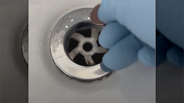 Person wearing blue glove using penny to scrap away limescale on sink faucet