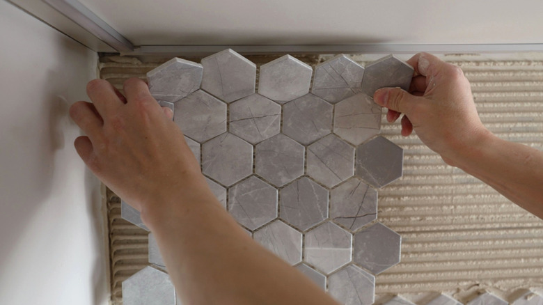 Someone installing gray backsplash
