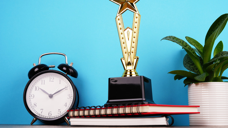 trophy on top of spirals on desk with plant and clock next to it