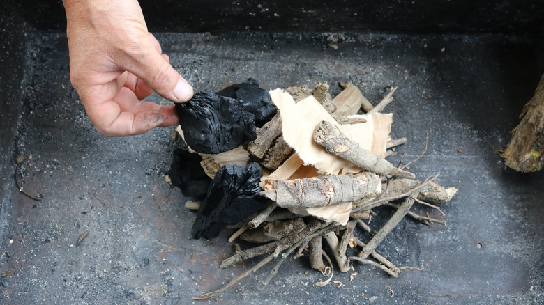 someone adding paper kindling to charcoal and twigs
