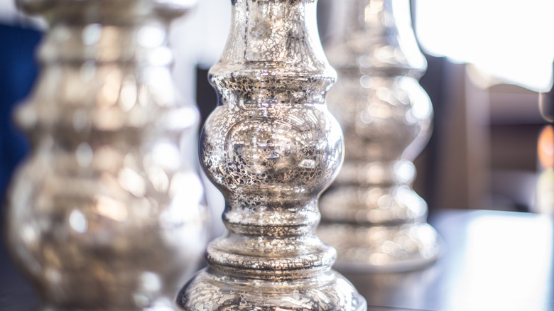 Three silver mercury glass vases stand on a tabletop.