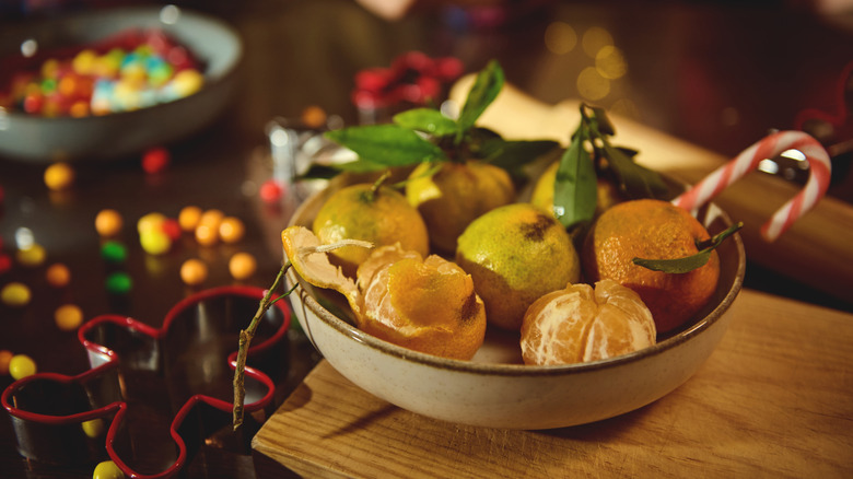 A wooden bowl is filled with citrus fruits and other Christmas items.