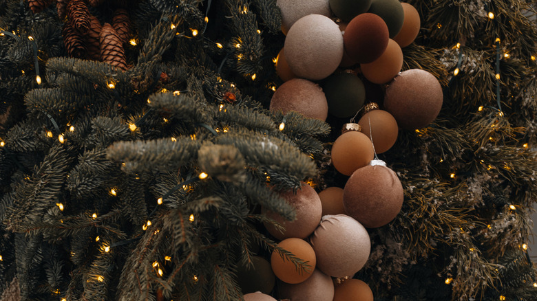A pine tree is decorated with lights and earth-tone fabric ornaments.