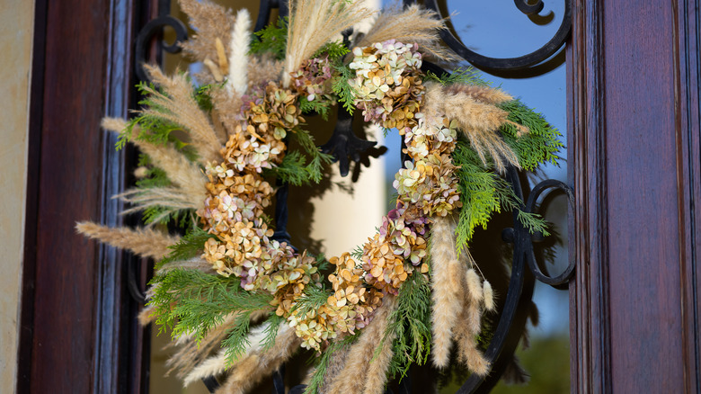 A wreath made from dried grasses, flowers, and cedar cuttings decorates a door.