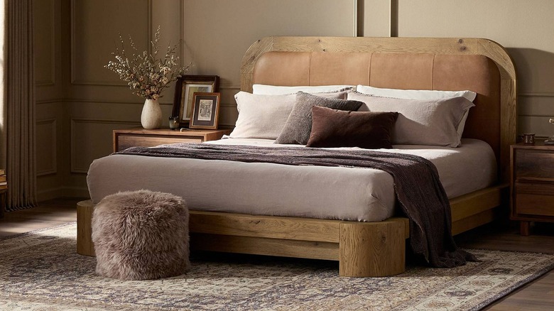 A wooden platform bed with a leather headboard and soft furnishings in various shades of brown and tan