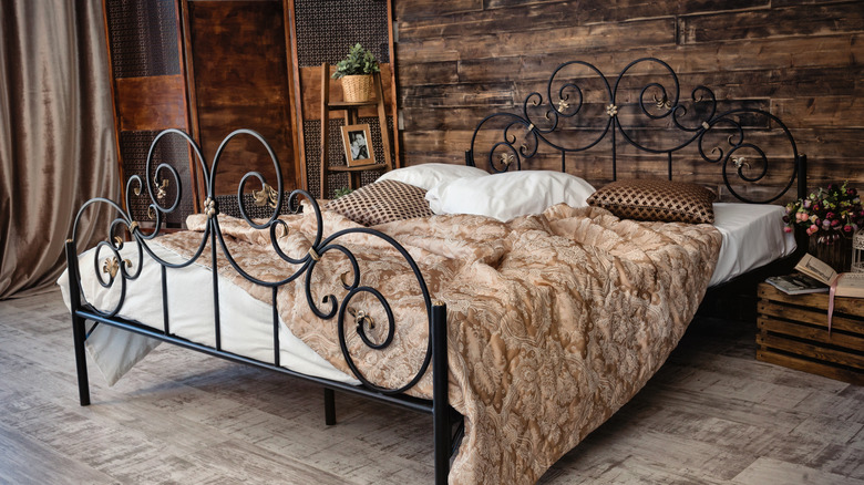 A stunning wrought iron bed in a rustic bedroom with dark wood paneling and pale wood flooring