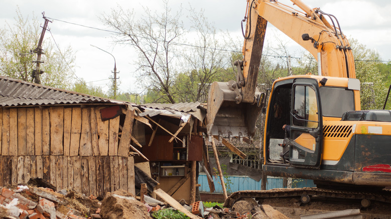 yellow excavator demolishes old buildings with its bucket