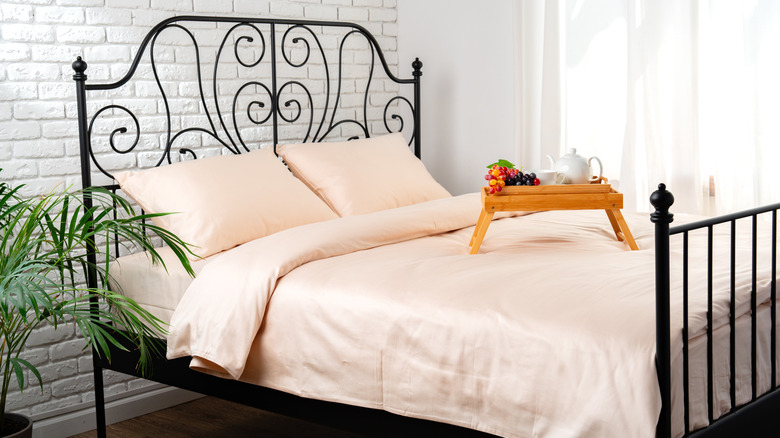 A light colored bed set with a wood tray on top