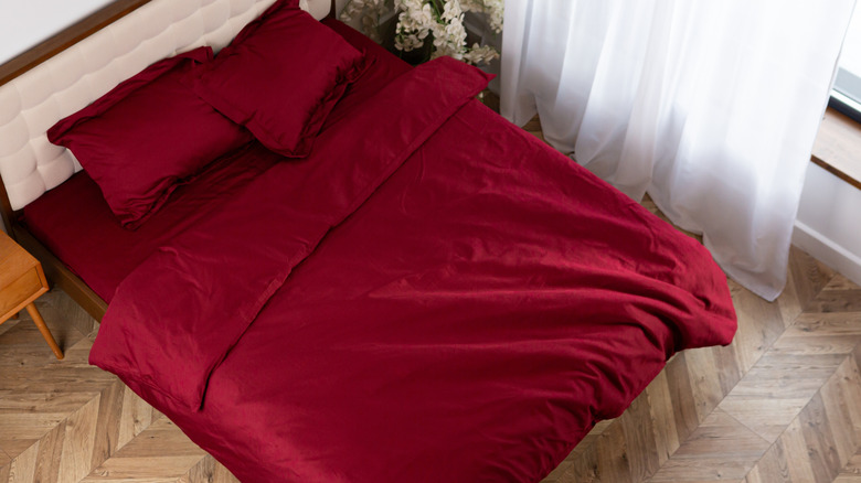 A zoomed out photo of a bed with a red satin bedding set