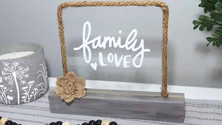 Clear glass sign with white lettering and rope trim on a wooden stand