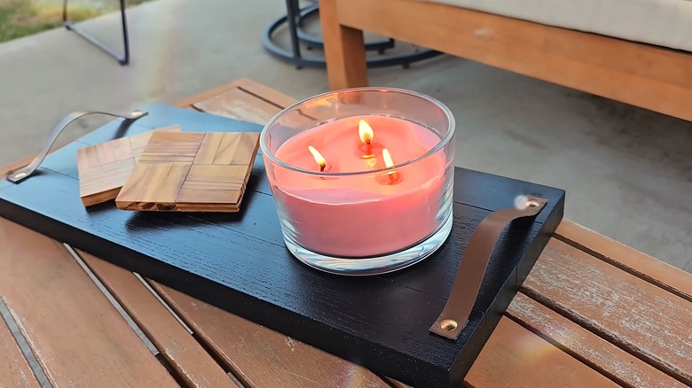 Black wooden plank tray with leather strap handles and coasters and a candle on top