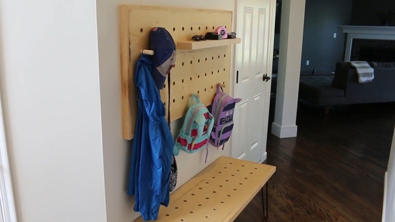 A large wood pegboard by the door holding a hat, bags, a jacket, and other accessories.
