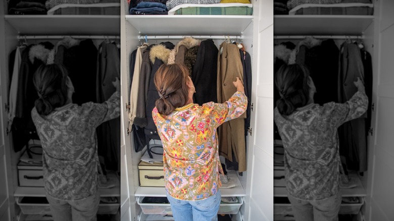 A woman looks through coats in a well-organized closet.