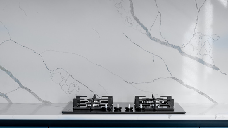 A gas stovetop with a marble splashback