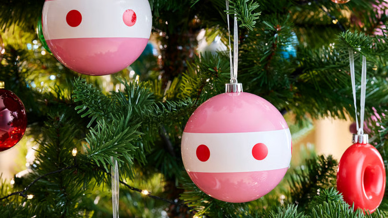 Two of the pink, red, and white mix patterns baubles hanging from a Christmas tree with lights and other baubles in the background