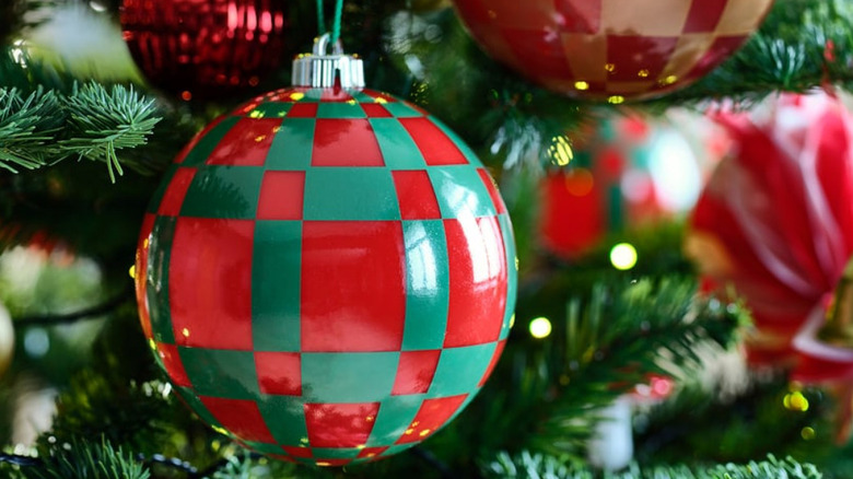 A green and red round Christmas ornament with other ornaments on a tree in the background