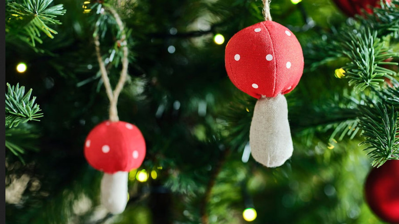 Fabric red mushrooms hanging from a Christmas tree with other red baubles and lights in the background