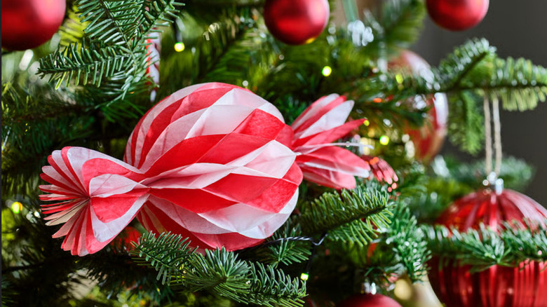 A paper red and white candy decoration sitting on a Christmas tree surrounded by other red ornaments