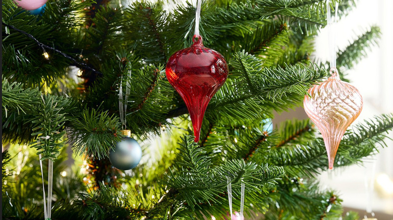 Red and pink ribbed ornaments hanging from a Christmas tree with ornaments in the background