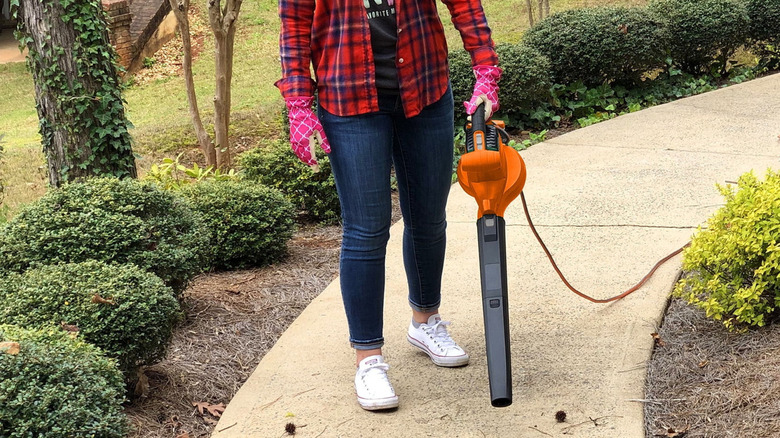Woman using the leaf blower to blow leaves from a walkway