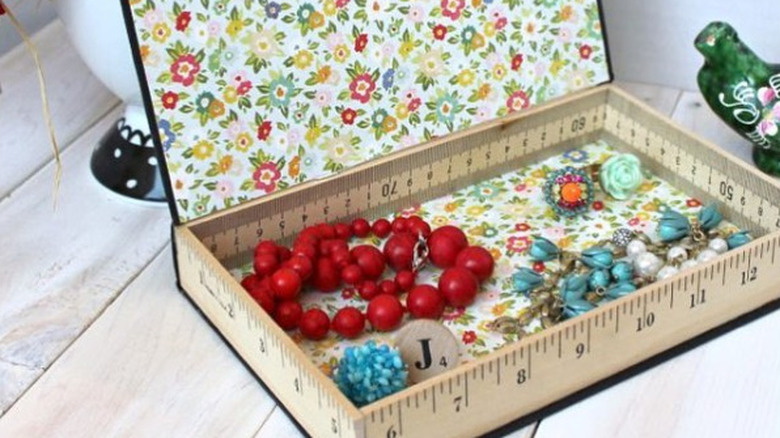 An influencer showcases the book cover she upgraded by lining it with a floral paper then creating a box by surrounding it with cut pieces of a yardstick.
