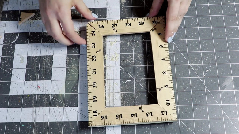 Person demonstrates a DIY picture frame using yardstick pieces that have been cut to smaller sizes and glued together
